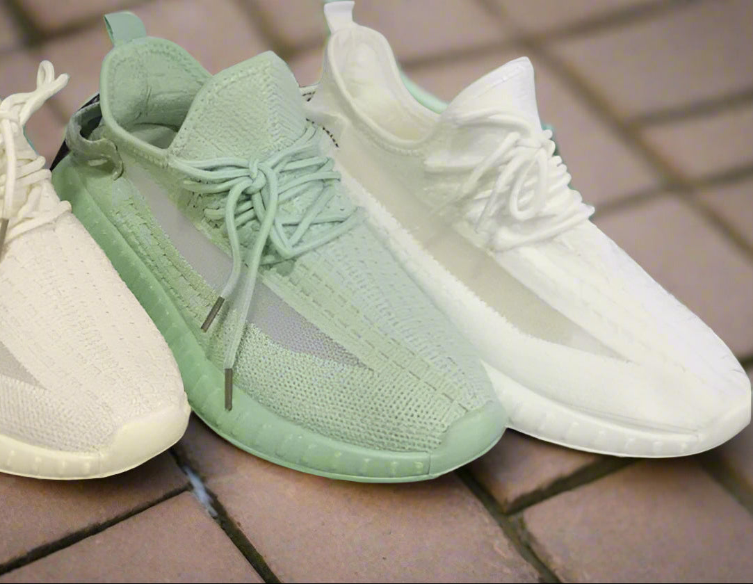 Four sneakers in black, white, green, and white on a gray surface.